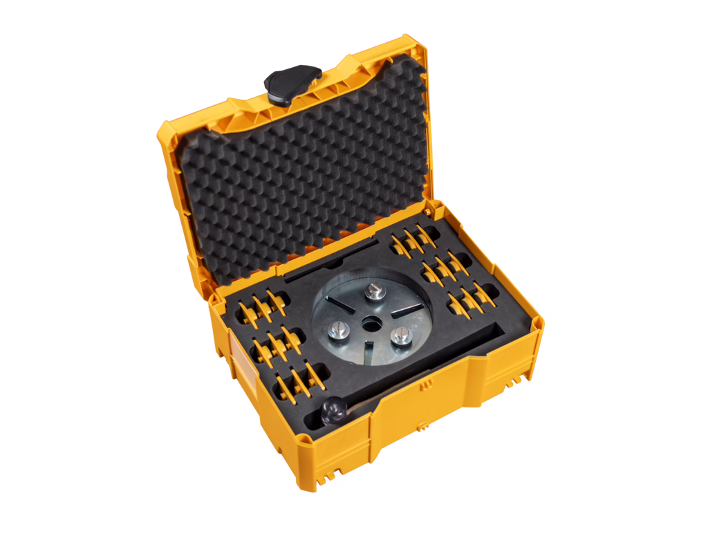 Coffret en plastique orange-jaune ouvert avec une mousse alvéolée dans le couvercle et des inserts en mousse sur mesure contenant une tête d'outil métallique ronde et plusieurs petits accessoires, photographié sur fond blanc.